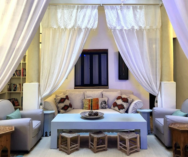 Riad Lyon-Mogador loungeruimte met witte gordijnen en Marokkaans decor.