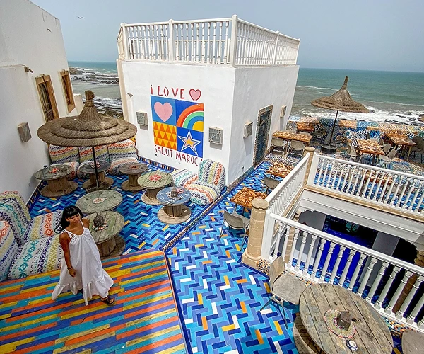Vrouw staand op het kleurrijke, betegelde dakterras van hotel Salut Maroc, met uitzicht op de oceaan.